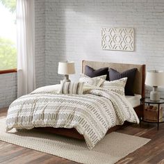 a bed in a room with white brick walls and wooden flooring next to a window