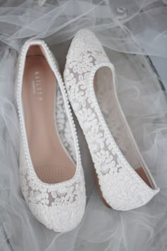 white wedding shoes with lace and pearls on the bottom are sitting on a veiled surface