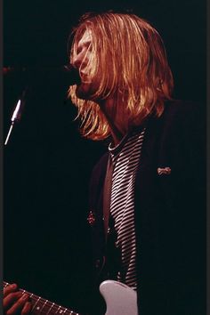 a man with long blonde hair playing an electric guitar at a music concert in front of a microphone