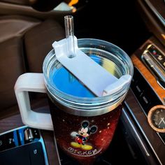 there is a cup with mickey mouse on it next to a car radio and steering wheel