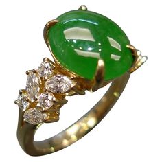 an oval shaped green jade surrounded by three small white diamonds in a yellow gold ring