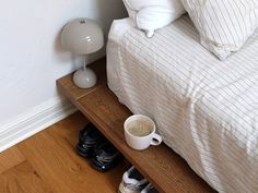 there is a coffee cup and some shoes on the floor next to a bed with white sheets