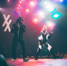 two young men standing on top of a stage with microphones in their hands and lights behind them