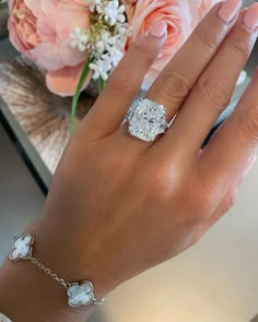 a woman's hand wearing a diamond ring and bracelet with flowers in the background