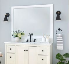 a white bathroom vanity with two black lights and a large mirror above it, next to a potted plant