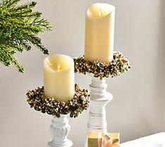 two white candles are sitting on a table next to a christmas tree and other decorations