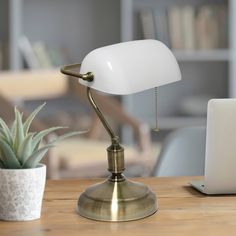 a desk lamp sitting on top of a wooden table next to a laptop and potted plant