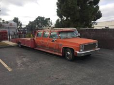 an orange pick up truck parked in a parking lot next to a fence and trees