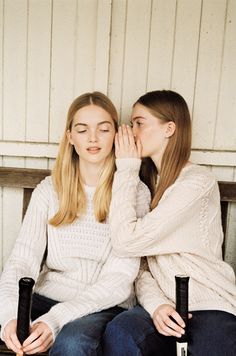 two young women sitting on a bench touching their noses with the other one's hand