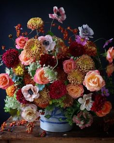 a vase filled with lots of colorful flowers on top of a wooden table in front of a black wall