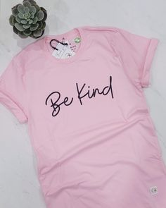 The pink 'Be Kind' t-shirt is a part of our Inspire Collection. It is a unisex classic fit, printed on a soft, ring spun cotton t-shirt. It features the classic script 'Be Kind' across the chest. Spread kindness with this casual staple, which is perfect for Pink Shirt Day Details: 100% ring spun cotton How this t-shirt fits: Fits true to size. Since it is a unisex classic fit, it can fit slightly loose and a little longer for women. Please refer to the sizing chart. How to care for your t-shirt: Machine wash in cold water, in a gentle cycle with like colours. Wash and iron garment inside out. Tumble dry on low Do not bleach Do not dry clean Do not iron over the design If unsure of sizes, please send us a message prior to placing your order. Basic Pink Pre-shrunk T-shirt, Pink Relaxed Fit T-shirt With Letter Print, Pink Slogan T-shirt With Short Sleeves, Casual Pink Slogan T-shirt, Pink Crew Neck Graphic Tee, Pink Graphic Tee With Crew Neck, Pink Relaxed Fit Pre-shrunk T-shirt, Trendy Pink T-shirt With Text Print, Pink Cotton Tops With Letter Print