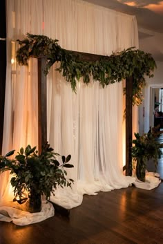 a room with white drapes and greenery on the wall