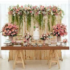 a table topped with lots of pink and white flowers next to a wall covered in greenery