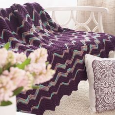 a crocheted blanket sitting on top of a bed next to a vase with flowers