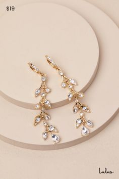 two pairs of gold tone earrings with clear crystal drops on each earring, sitting on top of a white plate