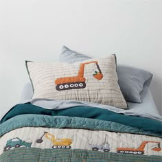 a bed topped with pillows and a quilted comforter covered in construction themed sheets