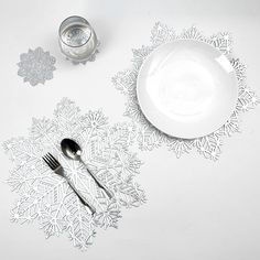 a white table with silverware and snowflakes on the placemats, next to a glass of water