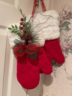 two red mittens hanging from a door with greenery on it and a pine cone in the middle