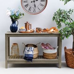 a table topped with baskets filled with food next to a wall clock and potted plant