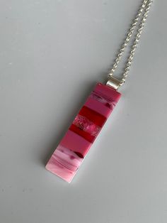 a pink rectangle pendant hangs from a silver chain on a gray surface with a white background