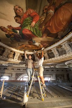 two men are painting the ceiling of a large building with paintings on it's walls