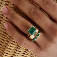 a person's hand with two rings on their fingers and one has a green stone