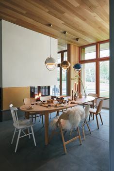 a dining room table with chairs and lights hanging from it's ceiling, in front of large windows