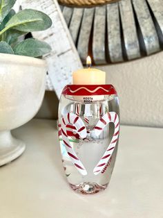 a glass candle holder with candy canes and a lit candle in the shape of a heart