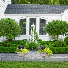 a white house with lots of trees and bushes around it's front yard area