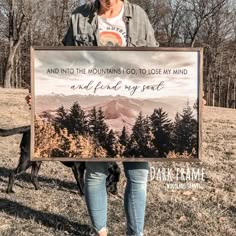 a woman holding up a sign that says and into the mountains go to lose my mind