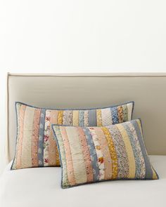 two pillows on a bed with white sheets and blue trimmings, one has a multicolored quilt