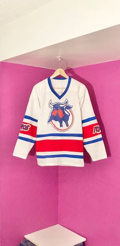 This jersey was made for former-WHA team the Toronto Toros. This jersey is the white home jersey for the team and has screenprint logos for the Toros and a screenprint #13 on the back. This is a mesh-style jersey as the pictures show. This jersey is in good condition with no rips, tears, or major stains. A handful of marks on back on bottom that were mostly removed. A few pinholes here and there as well. Overall great for a collector! Size: Size tag missing (probably about a Men's Small) 21" wid Graphic Print Jersey For Fan Apparel, Crew Neck Cotton Jersey With Team Logo, College Jersey With Team Logo And Crew Neck, Varsity Jersey With Team Logo And Crew Neck, White Sports Fan T-shirt For Fan Events, White Casual Jersey With Graphic Print, Casual White Jersey With Graphic Print, Varsity Jersey With Team Logo For Sports Season, Varsity Jersey With Team Logo