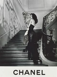 a black and white photo of a woman in a dress holding flowers on the stairs