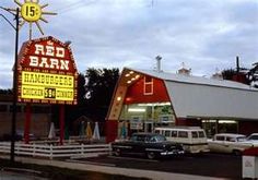 a red barn restaurant with cars parked in front of it and a large neon sign on the side of the building