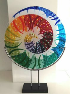 a colorful glass plate sitting on top of a black stand next to a white wall