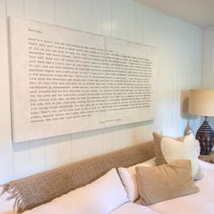 a bed with white sheets and pillows on top of it next to a wall mounted poem