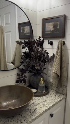 a bathroom sink sitting under a mirror next to a vase filled with flowers on top of a counter