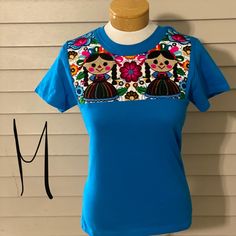 Embroidered Mexican T-Shirt Light Blue Short Sleeve Top With Floral Embroidery, Blue T-shirt With Embroidered Text For Spring, Blue Crew Neck Tops With Floral Embroidery, Blue Crew Neck Top With Floral Embroidery, Blue Crew Neck T-shirt With Embroidered Text, Blue Floral Embroidered Crew Neck Top, Casual Blue Top With Embroidered Text, Light Blue Embroidered Tops With Crew Neck, Short Sleeve Cotton Top With Machine Embroidery