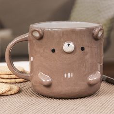 a coffee mug with a bear face on it sitting next to crackers and cookies