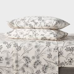 two pillows are stacked on top of each other in front of a bed with floral print