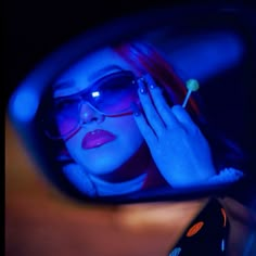 a woman wearing sunglasses is reflected in the rear view mirror of a car as she holds her hand up to her face