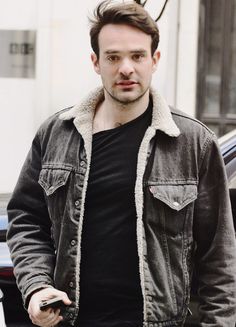 a man standing in front of a car holding a cell phone and looking at the camera