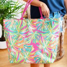 a person holding a colorful bag in front of a potted plant on the floor