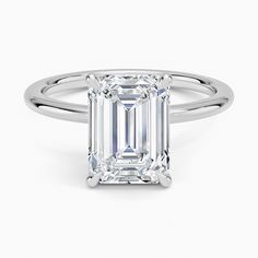 an emerald - cut diamond ring with three clawed shans on the band, set in 18k white gold