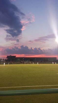 a baseball field with the sun setting in the background and people playing soccer on it