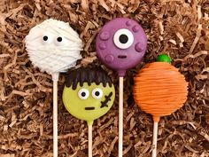 three halloween lollipops with faces on them sitting in some wood shaving