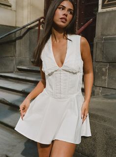 a woman in a short white dress posing for the camera with her hand on her hip