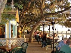 people are sitting at tables under umbrellas near the water