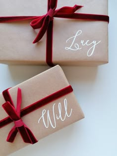 two wrapped gift boxes with red ribbon tied around the top and lettering on each box