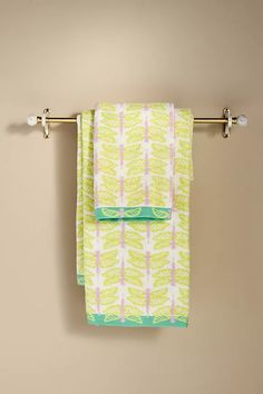 two towels hanging on a towel rack in front of a beige wall with green and white designs